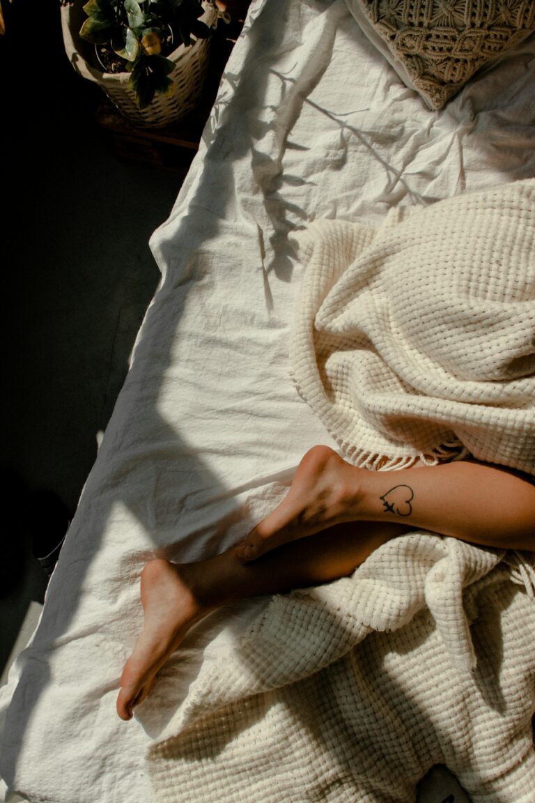 Relaxing scene of a sunlit bed with a cozy blanket and woman's leg visible, conveying warmth and comfort.